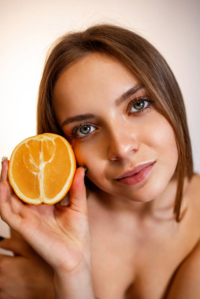 C-vitamiini iholle. Iloinen nuori kaunis nainen suljetuin silmin tilalla oranssi puoli yli vaaleanpunainen tausta - Valokuva, kuva