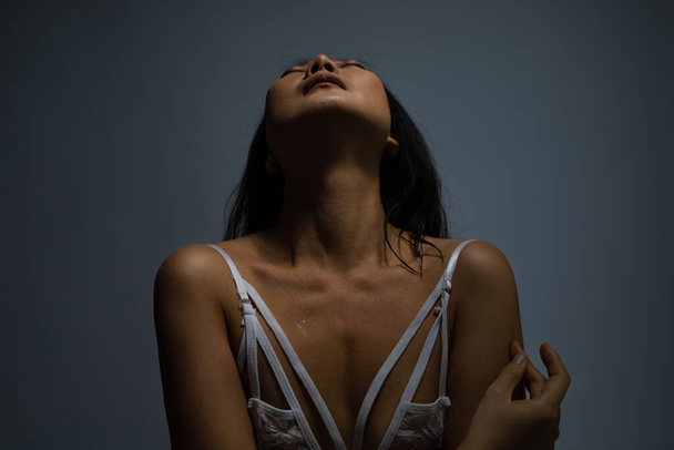Mooi Aziatisch meisje met sexy look in wit kanten ondergoed poserend over donkere achtergrond. Een studio opname. Fit body. - Foto, afbeelding