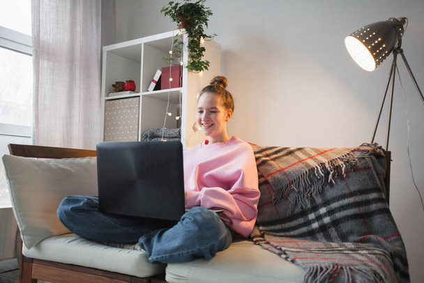 Relaxante jovem mulher usando laptop na sala de estar, trabalhando em projeto on-line, compras na internet Adolescente sentada no sofá, lendo e-mail, conversando em rede social, olhando para a tela, digitando - Foto, Imagem