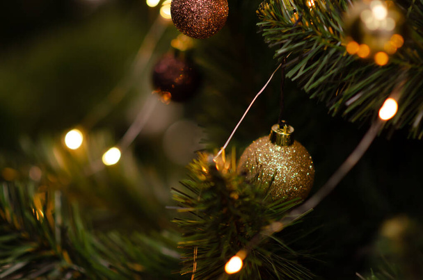 Traditional artificial Christmas tree with gold ball ornament and glowing colorful lights in background with copy space. Soft focus Christmas decorations. Seasonal winter holiday. New year concept. - Photo, image