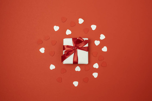 Geschenkkarton mit roter Schleife und Liebesform auf rotem Hintergrund. Ansicht von oben - Foto, Bild
