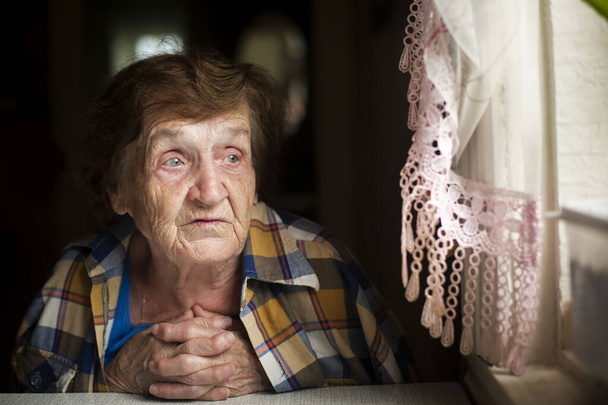 Une femme âgée s'assoit soigneusement à la fenêtre. - Photo, image