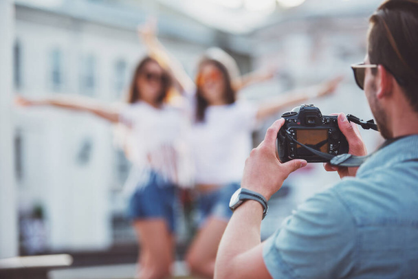 Freundschaft, Freizeit und Menschen. Rückansicht junger Mann fotografiert seine Freundinnen mit Fotokamera, im Freien, in der Stadt. - Foto, Bild