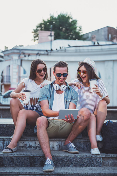 Дружба, досуг и люди концепции. Молодые люди хорошо проводят время вместе, используя цифровые планшеты, сидя на открытом воздухе, в городе
. - Фото, изображение