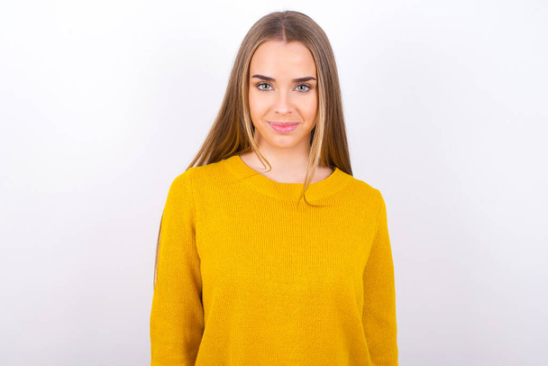 glimlachende jonge vrouw dragen gele trui poseren in studio - Foto, afbeelding