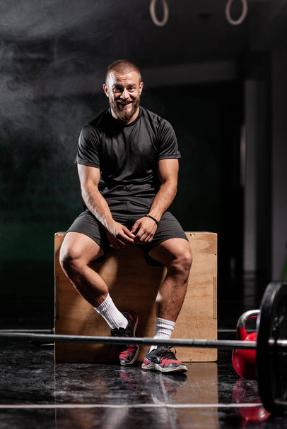 Muscular athlete posing with weightlifting equipment. Smoke background. - Photo, image