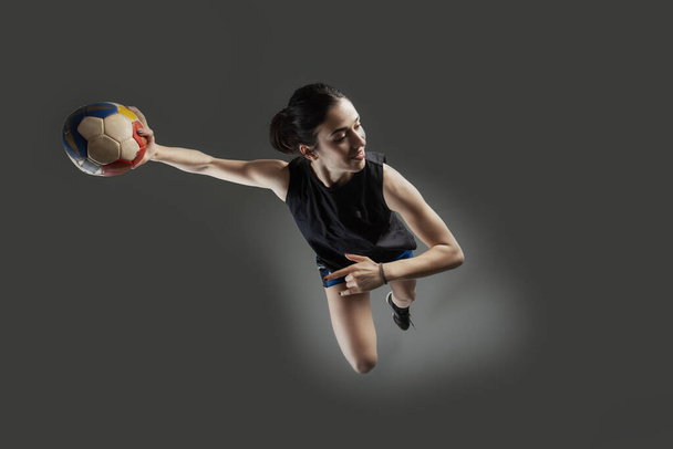 Handball player posing on gray background. Girl jumping with ball. - Fotó, kép