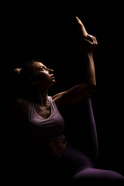 Fit girl practicing yoga in a studio. Half silhouette side lit fitness model - Zdjęcie, obraz