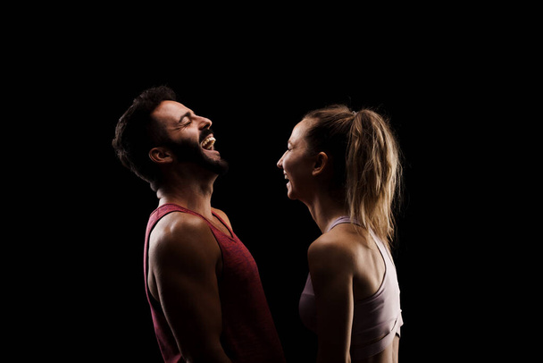 Fit couple posing together. Boy and girl side lit silhouettes on black background. - Фото, зображення