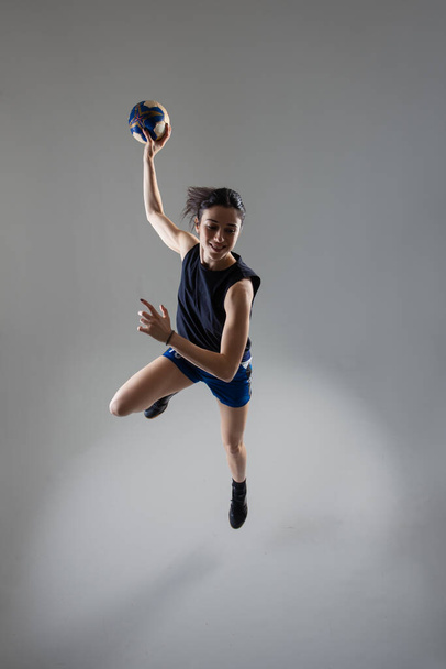 Handball player posing on light gray background. Girl jumping with ball. - Zdjęcie, obraz