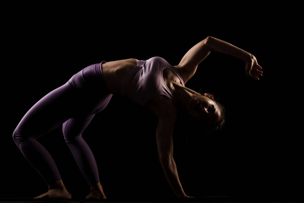 Fit girl practicing yoga in a studio. Half silhouette side lit fitness model - Valokuva, kuva