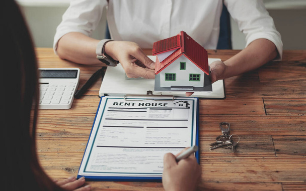 不動産業者や顧客は住宅購入契約に署名しています。ペンのサイン購入契約を保持する手。グレーの屋根の家と鍵が互いに近くに配置されます。 - 写真・画像