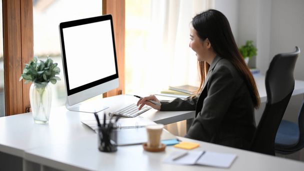 Succesvolle zakenvrouw, vrouwelijke financiële analisten of bankier werkt op desktop computer aan haar bureau. Computer blanco scherm mockup. - Foto, afbeelding