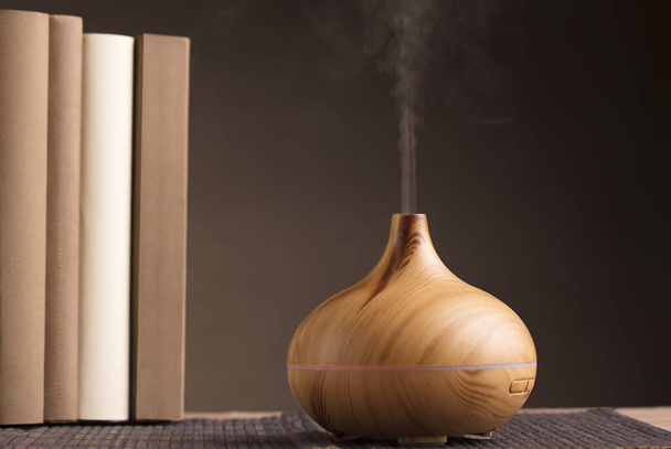 Esenciální olej osvěžovač vzduchu na dřevě, s knihami na stole, hnědé pozadí. - Fotografie, Obrázek