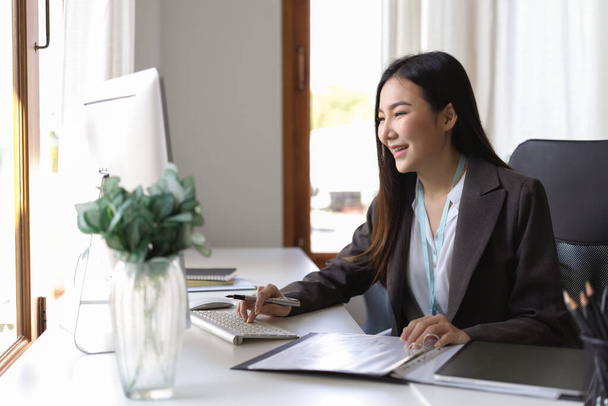 Junge asiatische Finanzmarktanalystin, die im Büro am Desktop-Computer arbeitet. Geschäftsfrau analysiert Dokument auf ihrem Schreibtisch. - Foto, Bild