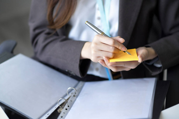 Imagem recortada de uma mulher de negócios tomando notas sobre nota pegajosa enquanto olha as informações sobre papeladas. - Foto, Imagem