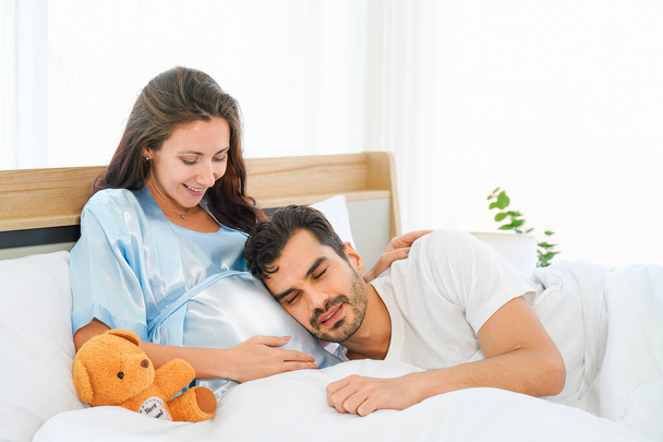 retrato de feliz esposa embarazada y marido acostados juntos en la cama en el dormitorio en casa - Foto, Imagen