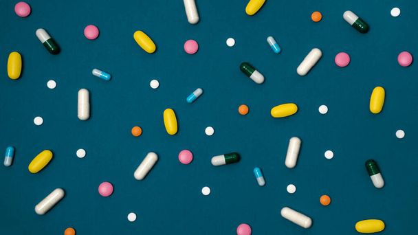 Banner mit blauem Hintergrund mit vielen Medikamenten in Kapseln und Tabletten in verschiedenen Farben auf der Oberfläche verstreut - Foto, Bild