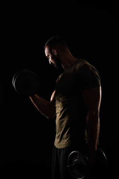 Portrait of handsome guy lifting weight while focusing on the muscles - Fotó, kép