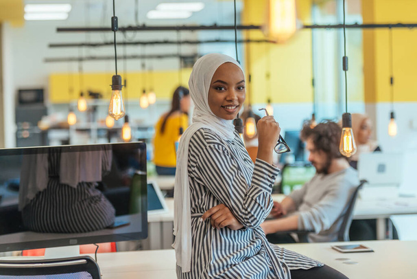 Retrato de una musulmana negra (afroamericana) parada en una moderna oficina de negocios mientras usa un hijab. - Foto, imagen