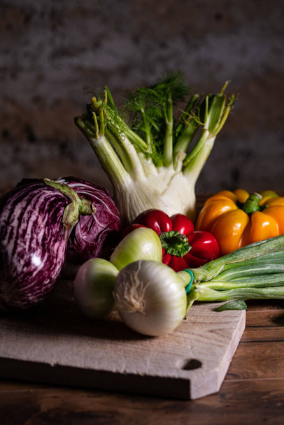 A vertical shot of a composition of vegetables with cutting board on wooden surface - Fotó, kép