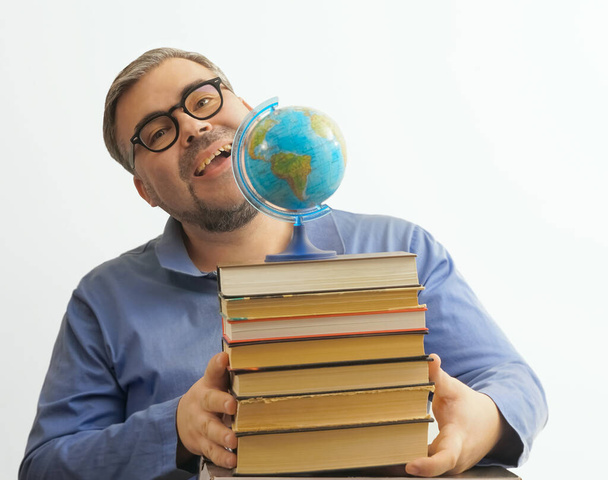 Bearded happy man with eyeglasses on white background holding  a globe in his hand while holding a stack of books - Foto, immagini