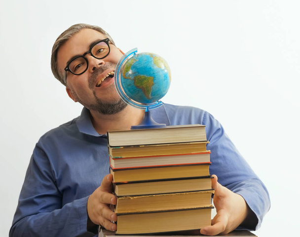Bearded happy man with eyeglasses on white background holding  a globe in his hand while holding a stack of books - Fotoğraf, Görsel