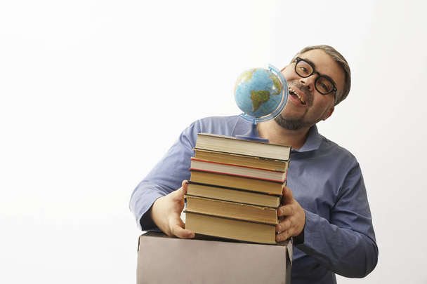 Bearded happy man with eyeglasses on white background holding  a globe in his hand while holding a stack of books - Fotografie, Obrázek