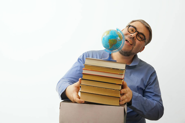 Barbuto uomo felice con gli occhiali su sfondo bianco che tiene un globo in mano mentre tiene una pila di libri - Foto, immagini