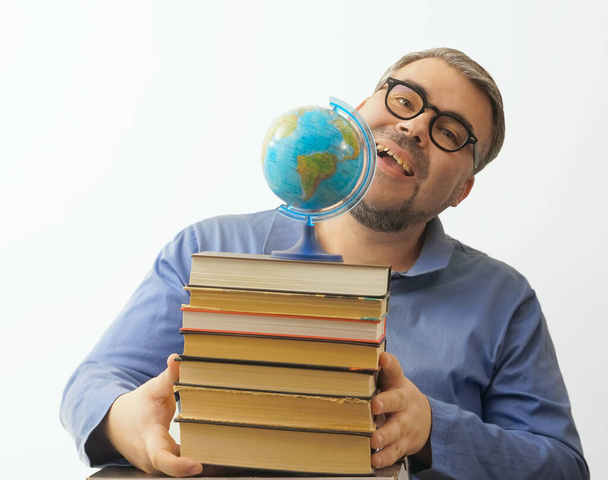 Bearded happy man with eyeglasses on white background holding  a globe in his hand while holding a stack of books - Zdjęcie, obraz