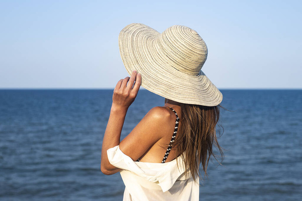 Nuori nainen hatussa kalliolla katselee merta kesäpäivänä  - Valokuva, kuva