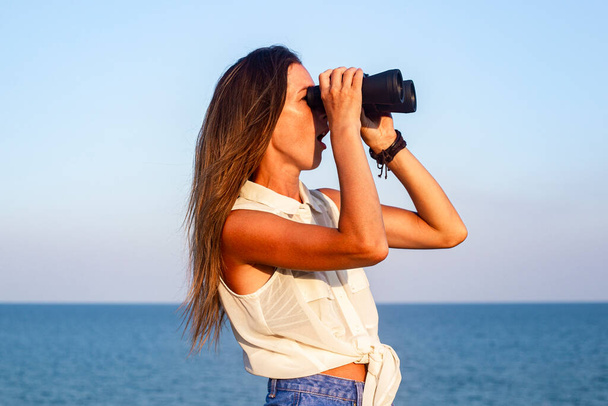 Mujer joven mirando a través de prismáticos en el mar desde el acantilado  - Foto, imagen