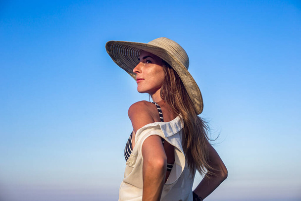 Young sexy woman in hat on blue sky background  - Foto, Imagem