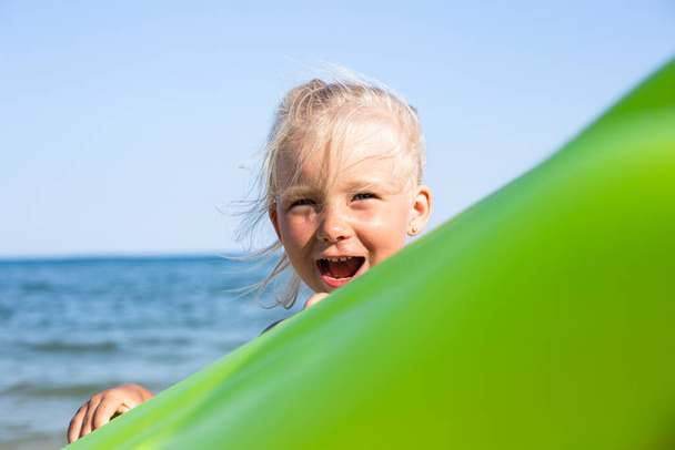 Wesoły uśmiech dziewczynka trzyma dmuchany materac na plaży  - Zdjęcie, obraz