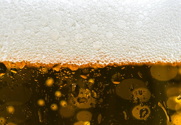 Um tiro de close-up de um copo transparente cheio de cerveja gelada e sua espuma na parte superior - Foto, Imagem