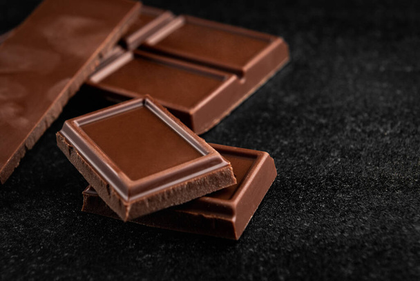Stukken melkchocolade op zwarte achtergrond. - Foto, afbeelding