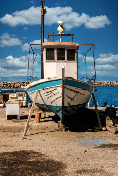 A vertical shot of an old weathered grungy fishing boat under a blue cloudy sky on a sunny day - Zdjęcie, obraz