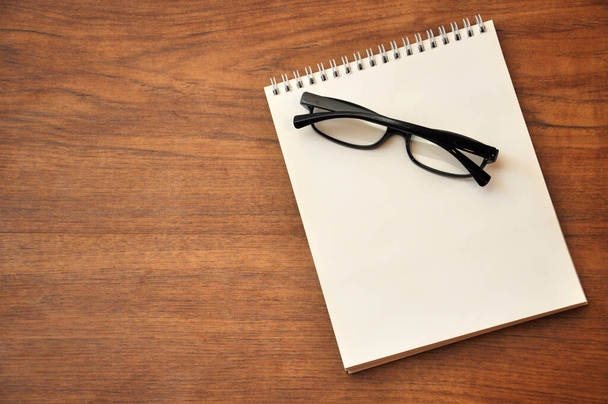 Black eyeglasses on a spiral notepad . A person's workspace is an office desk on top. Copy space. - Photo, Image