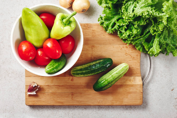 Légumes frais sur une planche à découper. Ingrédients pour la fabrication de salade, tomates, concombres, poivrons, laitue, oignons et ail. - Photo, image