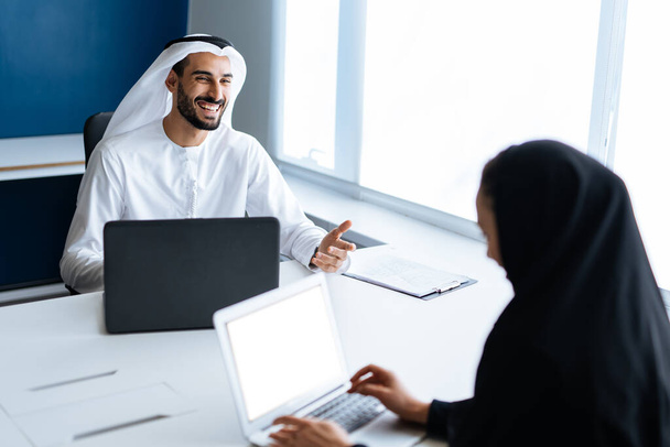 Man and woman with traditional clothes working in a business office of Dubai. Portraits of  successful entrepreneurs businessman and businesswoman in formal emirates outfits. Concept about middle eastern cultures, lifestyle and professional occupatio - Fotoğraf, Görsel