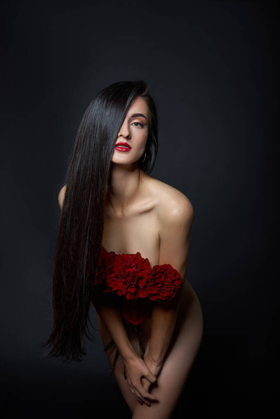Beautiful brunette woman with a bouquet of red rose flowers in red corset. Long hair, nude slim body art portrait - Fotó, kép