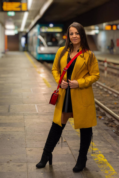 A vertical shot of a stylish young female with a yellow coat at a subway station - Foto, imagen