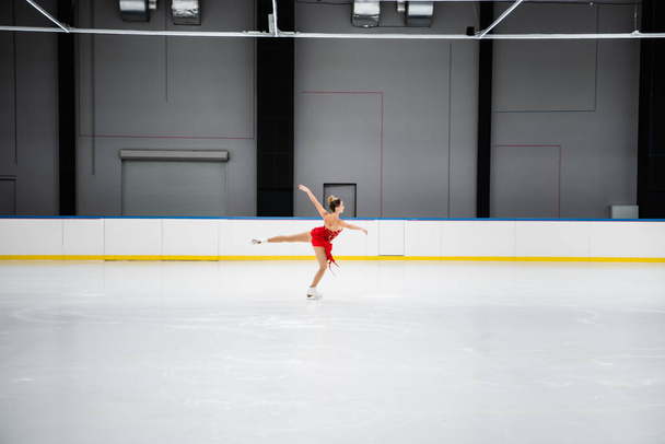 full length of figure skater in dress performing camel spin in professional ice arena - Foto, Bild