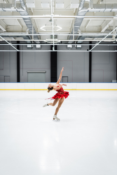 full length of young woman bending while figure skating in professional ice arena - Foto, Bild