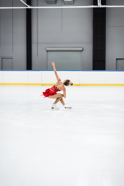 full length of young woman with outstretched hand figure skating in professional ice arena - Foto, Bild