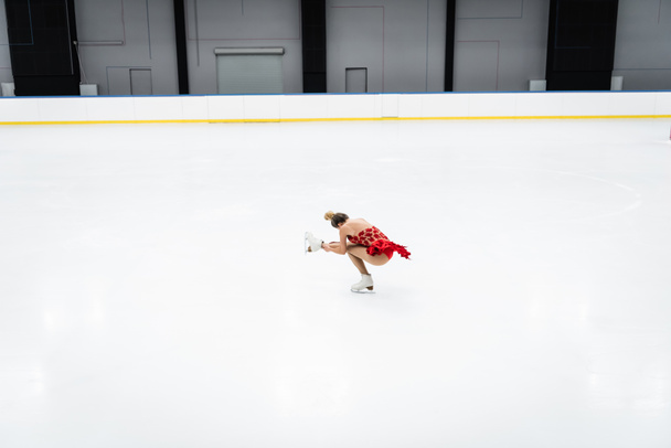 full length of woman in dress performing sit spin in professional ice arena - Valokuva, kuva