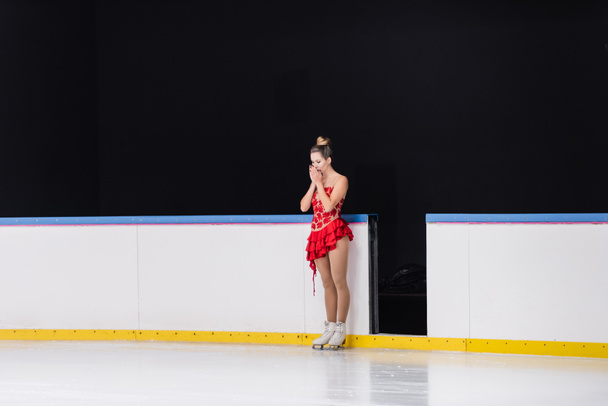 pełna długość zmartwionej łyżwiarki figurowej w czerwonej sukience stojącej na lodowisku  - Zdjęcie, obraz