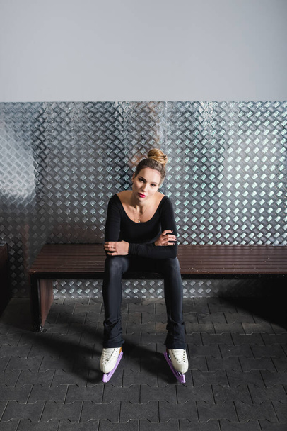 comprimento total da jovem mulher em patins figura branca e bodysuit preto sentado no banco  - Foto, Imagem