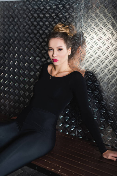 full length of young figure skater in black bodysuit sitting on bench  - Photo, Image