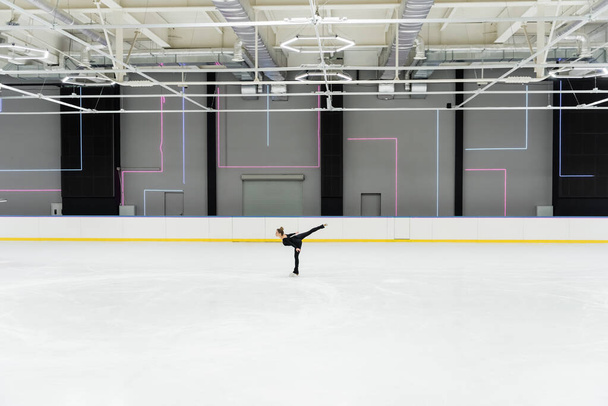 side view of figure skater in black bodysuit skating in professional ice arena - Foto, Imagen